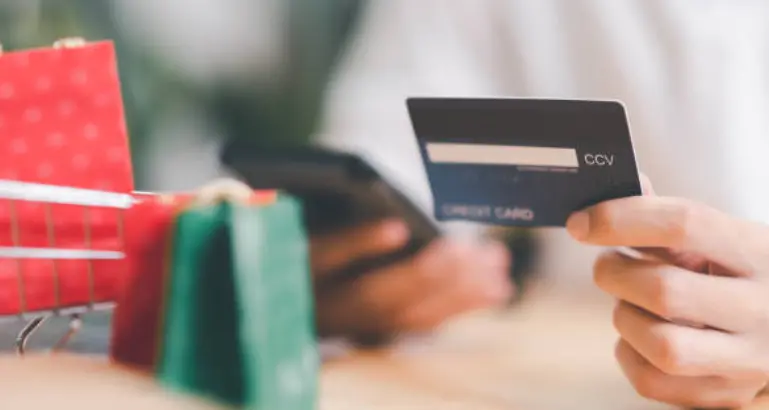 A person holding a bank card in one hand and a phone in the other hand to perform a transaction or check the expenses.
